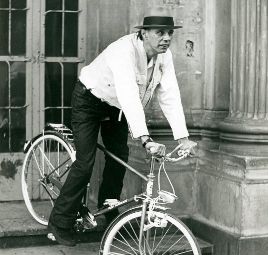Joseph Beuys – mit Fahrrad auf den Stufen des Haupteingangs der Kunstakademie Düsseldorf, aus Bestand: AEKR Düsseldorf 8SL 046 (Bildarchiv), 019_0073. Ausschnitt. Foto: Hans Lachmann, Lizenz: CC BY-SA 2.0, Quelle: Wikimedia Commons